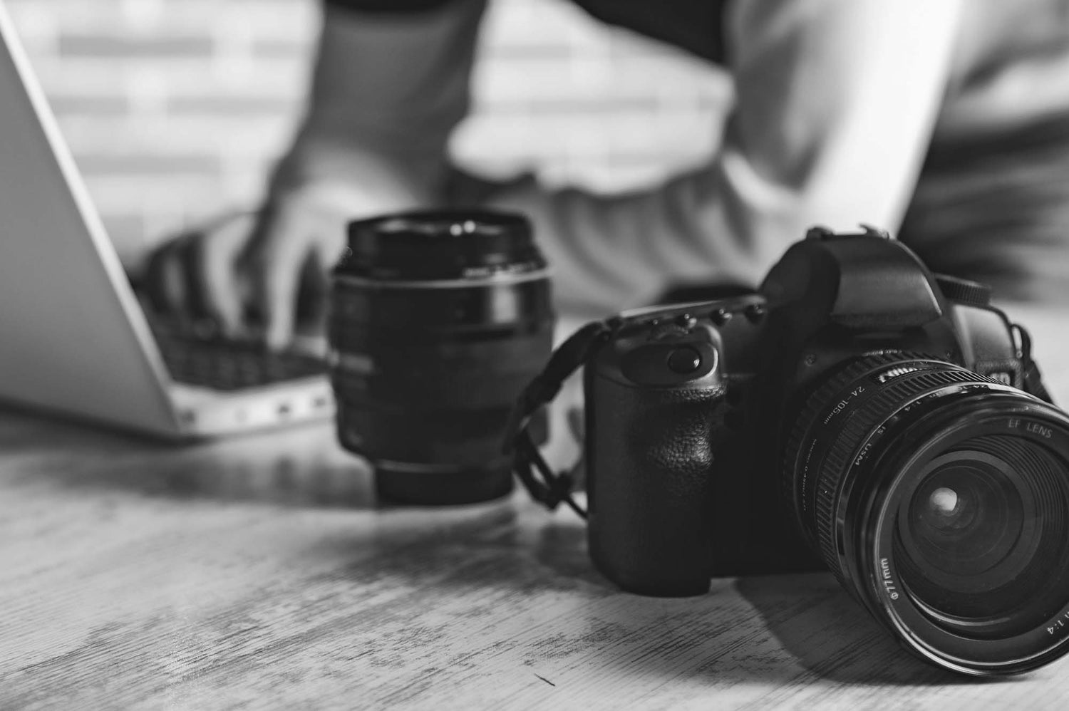 Camera and lens on a table with a person using a laptop in the background